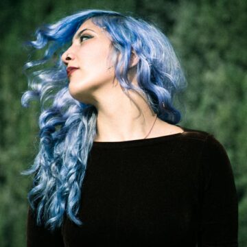 Portrait of Kimiya Khosrovani with blue hair, posing against a green background in Tustin, CA, created by Coldea Productions.