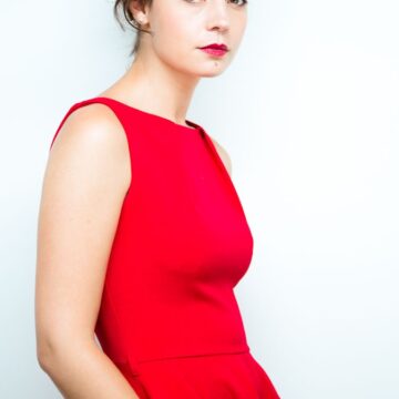 Maria-Dinulescu A professional headshot of a woman in a striking red dress against a clean, light background, showcasing headshot photography.