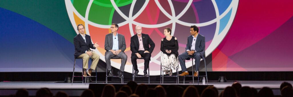 Event-Photography A panel discussion with five speakers on stage at a convention event, with colorful branding in the background at Moscone Center.