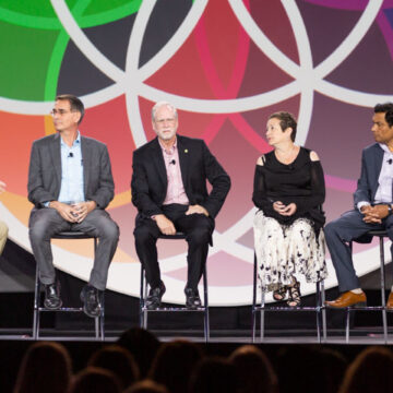 Event-Photography A panel discussion with five speakers on stage at a convention event, with colorful branding in the background at Moscone Center.