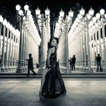 A dancer striking an elegant pose at night amidst the illuminated installation of "Urban Light" at LACMA, blending fashion, dance, and portrait photography by Coldea Productions.