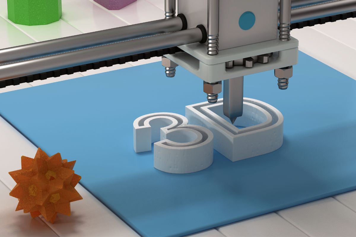 A 3D printer creating the text 3D on a blue platform, with a green hexagonal object, a purple square, and an orange star-shaped object nearby.