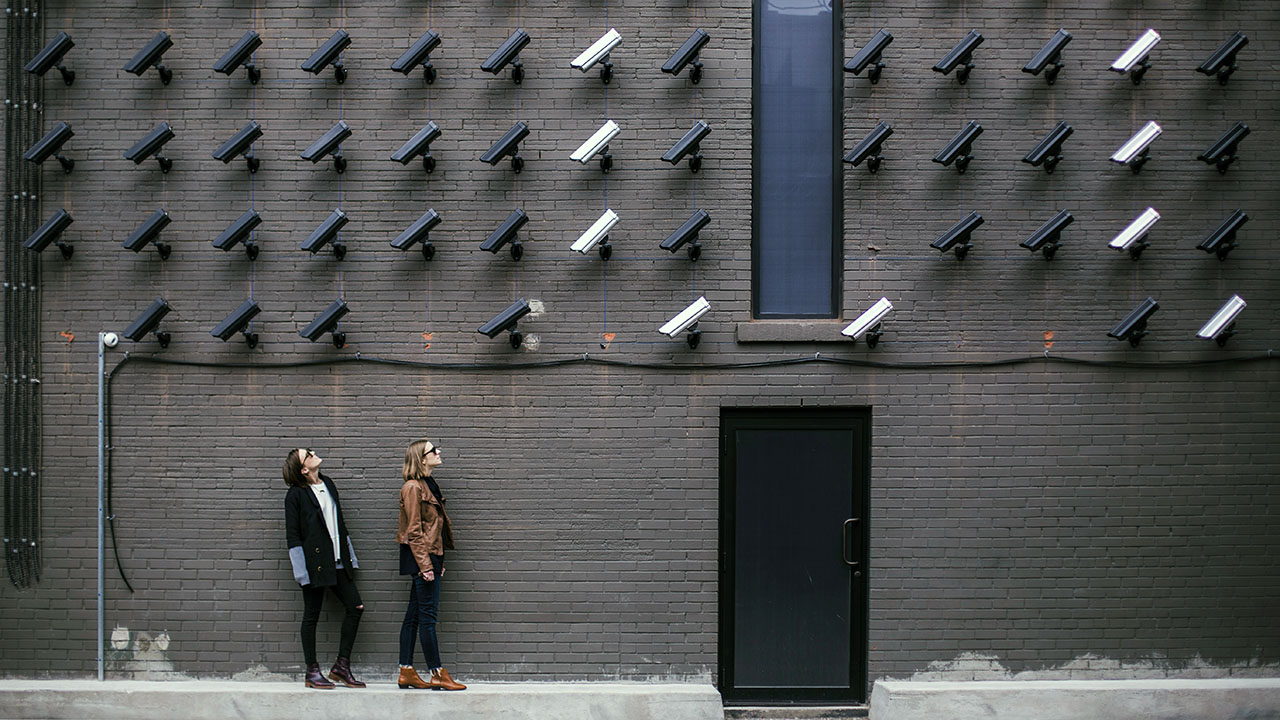 Two individuals standing in front of a wall covered with surveillance cameras, symbolizing the importance of branding a business as secure and confidential.