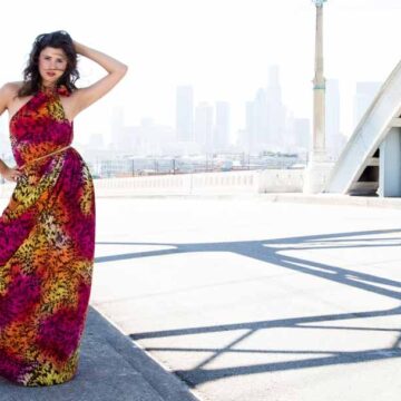 A woman in a vibrant, colorful dress posing confidently on the 6th Street Bridge in Los Angeles, with the city skyline in the background, showcasing fashion photography.