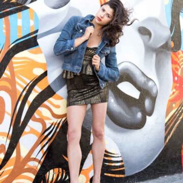 Fashion portrait of a woman in a denim jacket and patterned dress posing confidently against a colorful mural in the Arts District, Los Angeles, captured by Coldea Productions