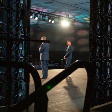 Convention-Photography Two presenters on stage viewed from behind the scenes, with large LED screens framing the stage during a live event.