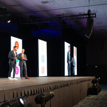 Convention-Photography Camera operator filming presenters discussing product features on stage at the Scentsy conference, captured by Coldea Productions, highlighting professional event video production.