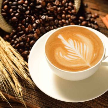 Food Product Photography Cup of latte with latte art surrounded by coffee beans, wheat stalks, and cinnamon sticks, captured by Coldea Productions’ product photography services