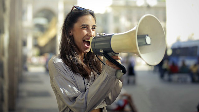 A happy young woman shouting through a megaphone