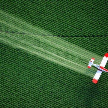 Aerial view of a crop-dusting airplane flying over green farmland, captured by Coldea Productions’ drone photography services.