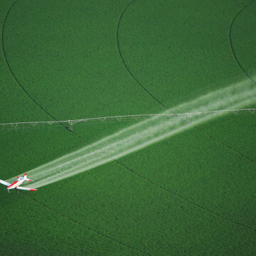 Aerial view of an agricultural field with a crop-dusting plane spraying crops, demonstrating Coldea Productions' drone and aerial photography services.
