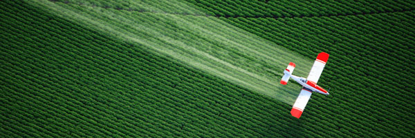 An aerial view of a crop-dusting plane flying over a green field, representing Coldea Productions' expertise in aerial drone video production.