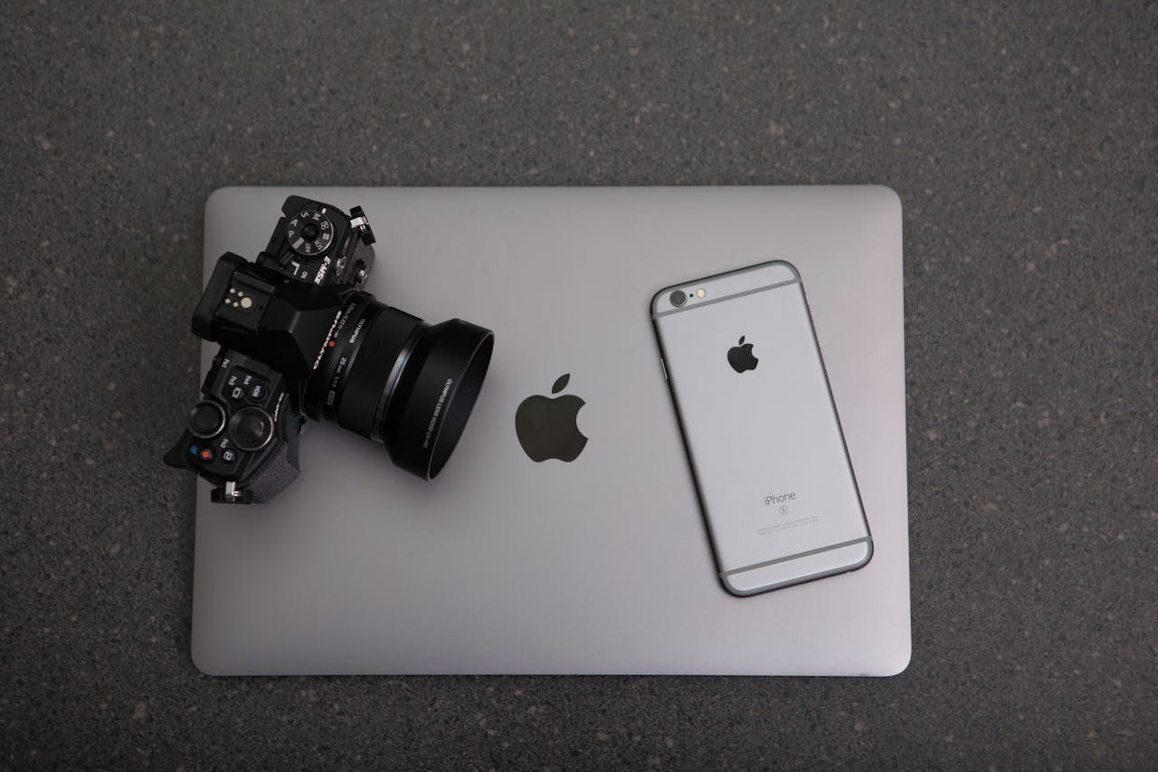 A camera and a phone on a laptop that is placed on a black surface.