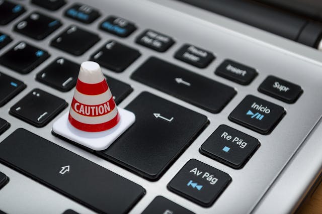 Mini caution cone placed on a laptop keyboard symbolizing phishing risk awareness.