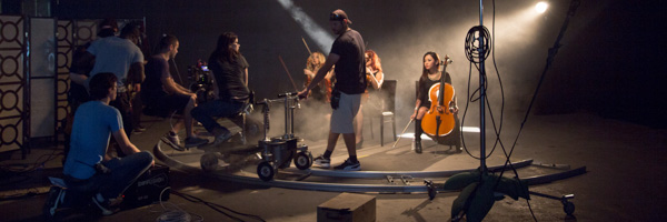 Film crew using a camera dolly to capture musicians playing string instruments on a smoke-filled set.
