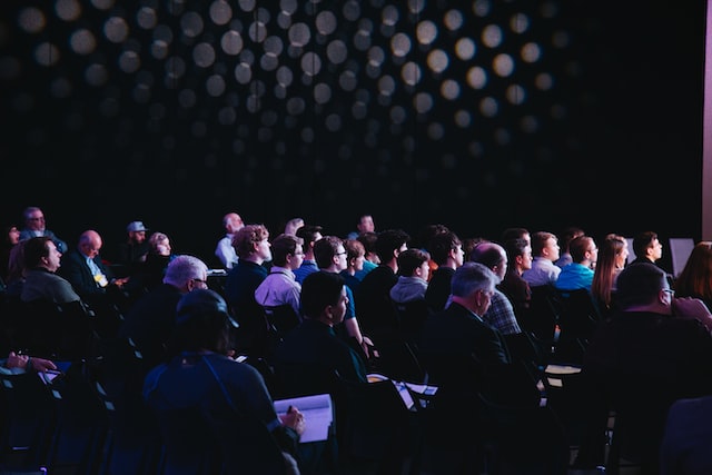 Audience seated in a conference setting, attentively listening to a presentation.