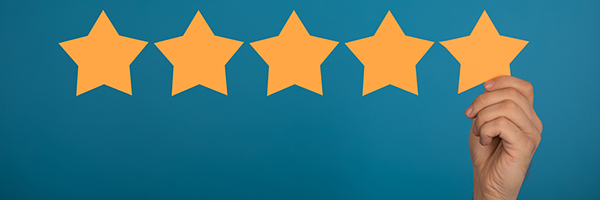 Hand placing a fifth star on a row of five yellow stars against a blue background, representing a five-star rating.