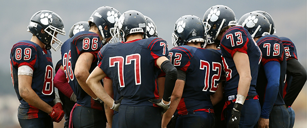 High school football team in huddle preparing for gameplay, ideal for athlete recruiting video highlights.