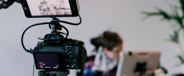 Close-up of a camera recording a live-streamed event with a person using a tablet in the background, produced by Coldea Productions.