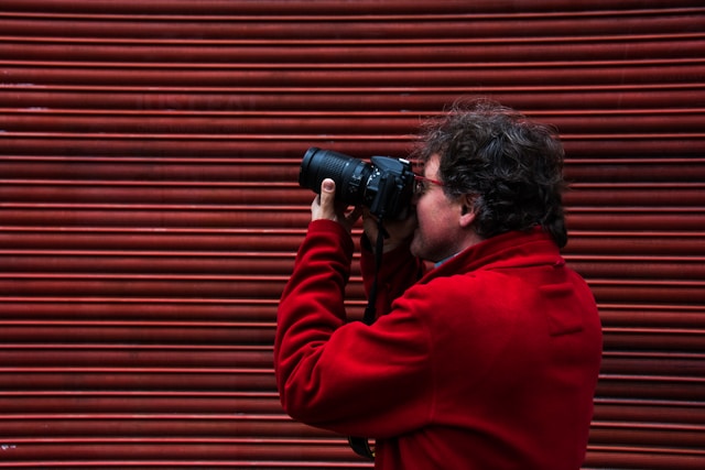 Local photographer in a red jacket taking a photo against a red urban wall, representing how local expertise adds authenticity and character to professional photography by Coldea Productions.