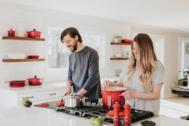 A young couple cooking together in a modern kitchen with white interiors and red accents, highlighting a warm and stylish home lifestyle.