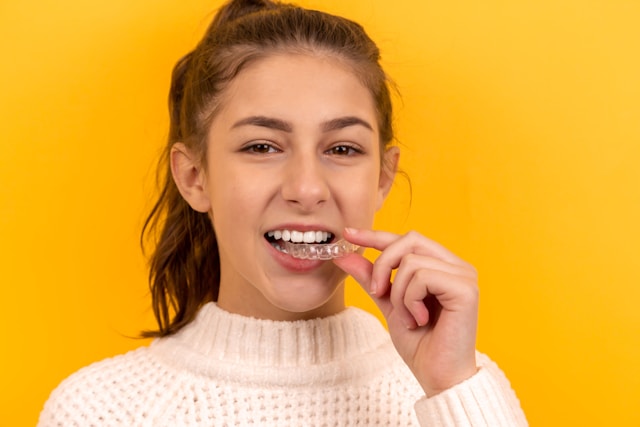 Teenage girl smiling while placing a clear orthodontic aligner on her teeth, symbolizing real orthodontic patient journeys in NYC healthcare marketing.