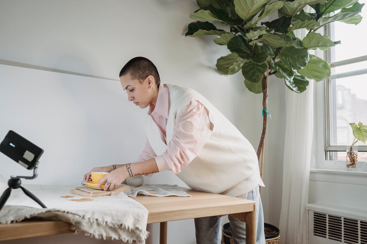 Person arranging a yellow cup on a styled table while recording content with a smartphone on a tripod