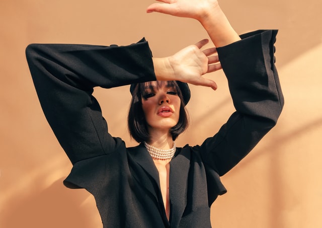 Stylish portrait of a model in a black outfit and pearl necklace, posing against a neutral background, illustrating fashion product photography tips to boost sales.