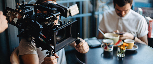 A videographer using professional equipment to capture a product demo scene in a casual setting with a person in the background.