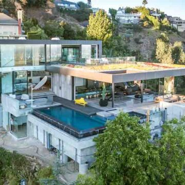 Aerial view of a modern luxury hillside home with an open terrace, pool, and glass walls, showcasing Coldea Productions' real estate photography skills