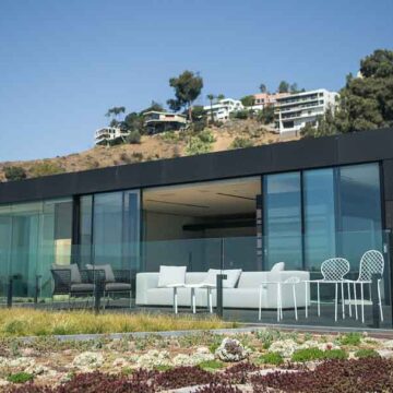 Modern hillside home with large glass walls and an outdoor seating area, showcasing Coldea Productions' real estate photography services.