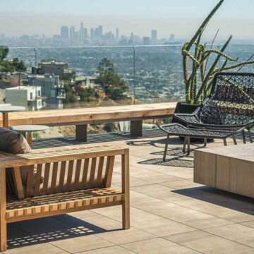 A rooftop patio with modern wooden seating, offering panoramic views of the Los Angeles skyline, captured by Coldea Productions for real estate photography.