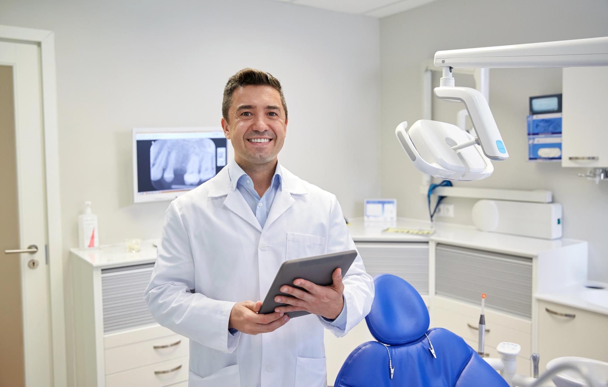 Dentist standing in a modern dental office holding a tablet, ready to welcome patients