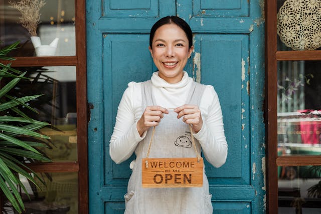 Smiling small business owner holding an open sign, representing trust and cybersecurity protection.