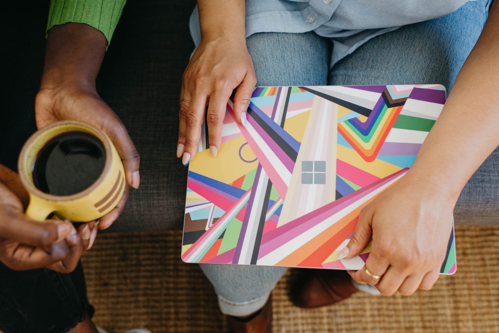 Two people sharing a moment with one holding a colorful laptop and the other holding a coffee cup.