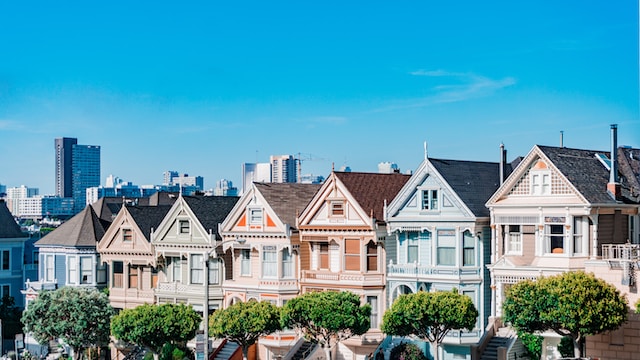 A row of colorful Victorian-style homes, known as the Painted Ladies, with the San Francisco skyline in the background on a clear day.