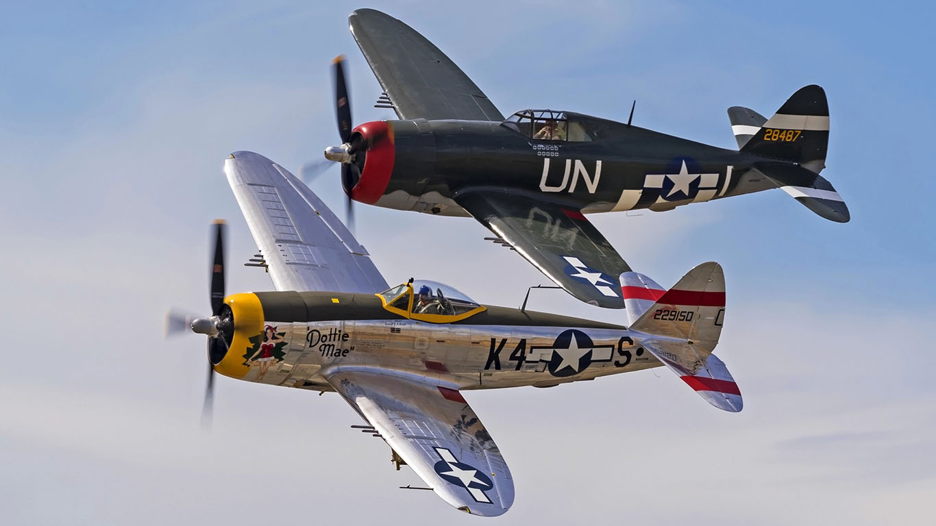 Two vintage World War II fighter planes in flight during an airshow, with clear blue skies in the background.