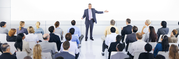 A professional speaker addressing a diverse audience during a corporate training session in a modern white auditorium.