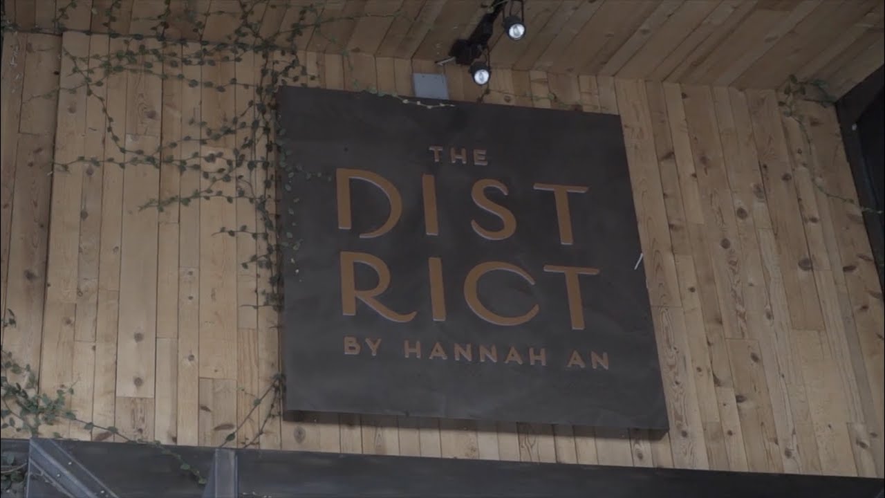 The District by Hannah An restaurant sign with wood backdrop, showcasing the elegant branding of this dining location in a video presentation by Coldea Productions.
