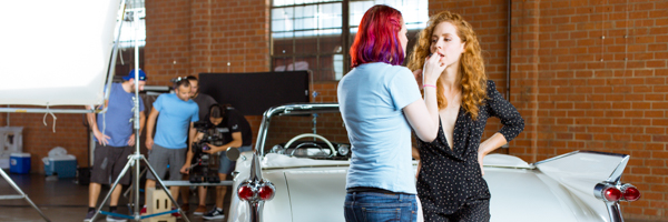Behind-the-scenes of a video production shoot in Santa Monica, California, featuring a makeup artist preparing an actress in front of a vintage car.