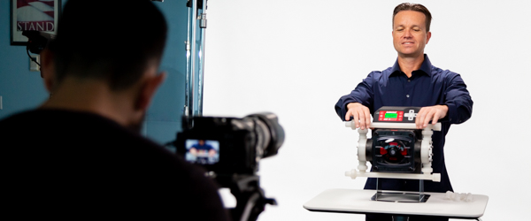 Rob Gledhill from Blue-White Industries demonstrates the functionality of a Plastic Chemical Feed Skid while Alexis Mendez from Coldea Productions captures the presentation on video.