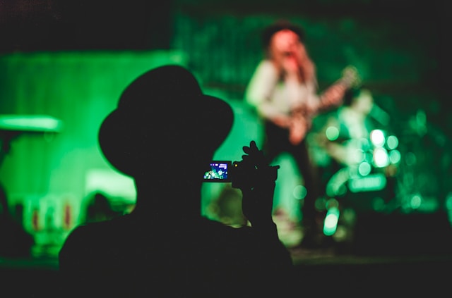 Silhouette of a person recording a live concert on their DV Camcorder Mini Camera, symbolizing video production for events on a budget.