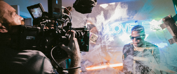 Cameraman filming a performance with neon lighting and creative props, including dollar bills and reflective surfaces.