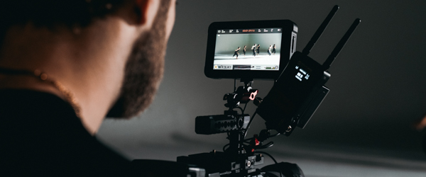 A videographer filming a group of dancers, capturing the scene on a professional camera monitor.