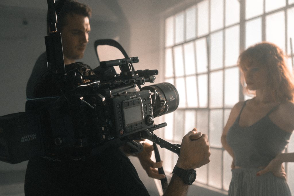 Behind-the-scenes shot of a videographer filming a model with professional camera equipment.