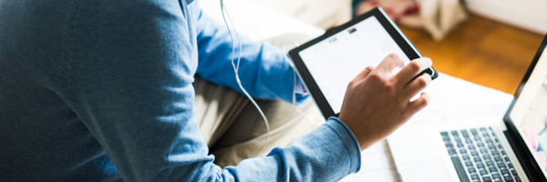 A person using a tablet while working on a laptop, representing Coldea Productions' expertise in producing web videos for online engagement.