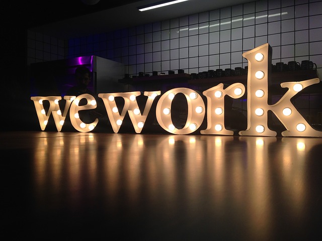 Illuminated "WeWork" sign on a reflective surface in a modern workspace setting.